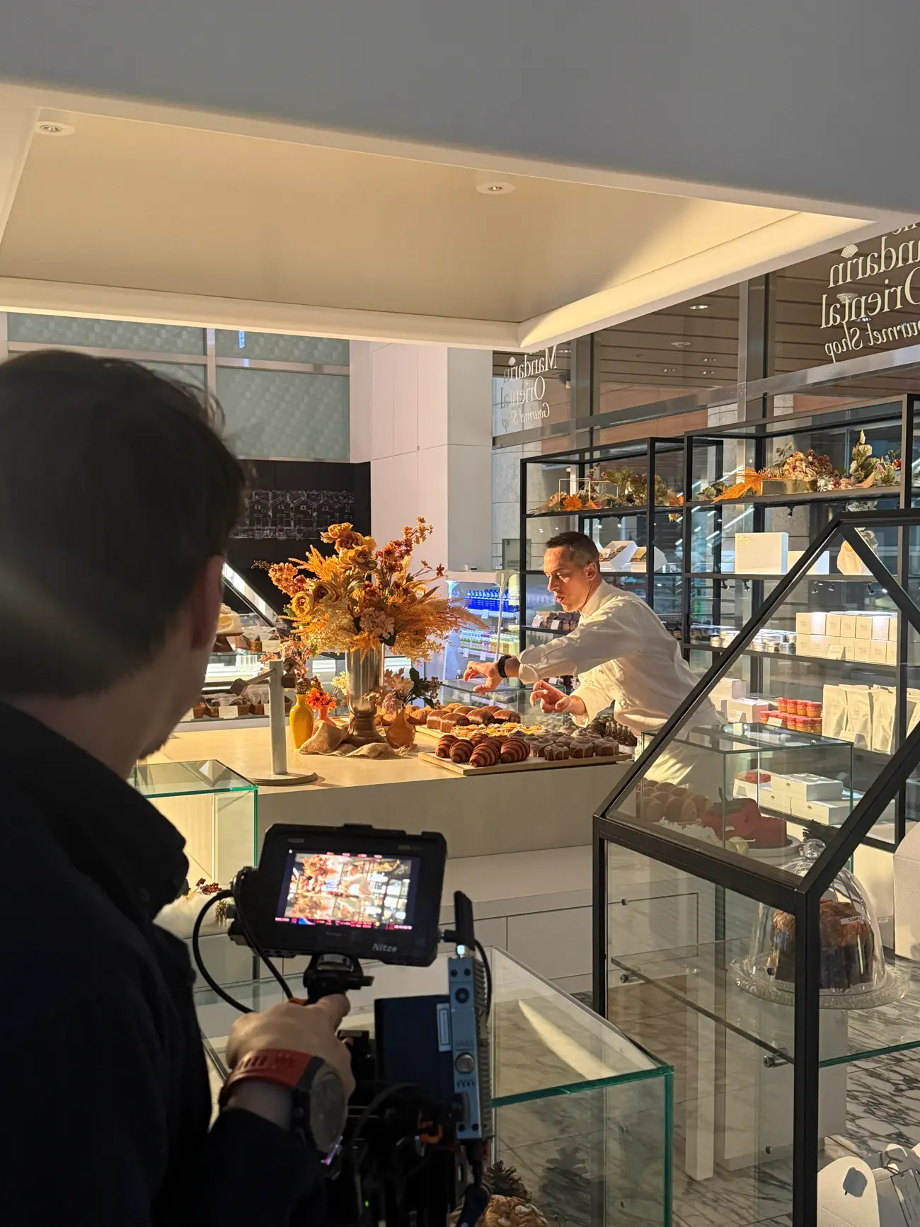 A camera operator filming a pastry counter inside a hotel food shop