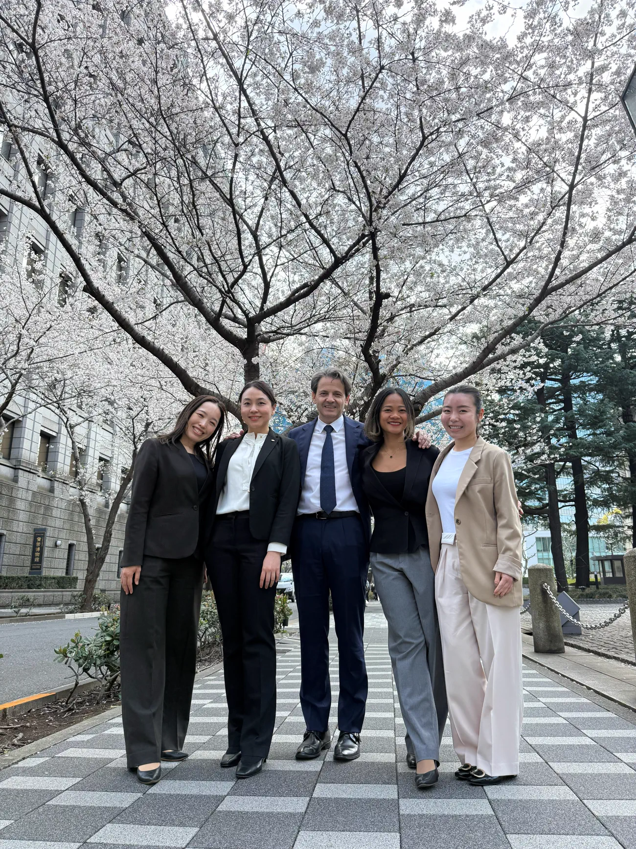 Five colleagues standing together beneath cherry blossom trees